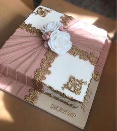 a pink and white cake with gold trimmings sitting on top of a table