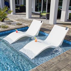 two white lounge chairs sitting on top of a pool