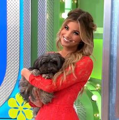 a woman in a red dress holding a dog on the set of tv talk show