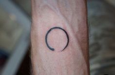 a small black circle tattoo on the wrist