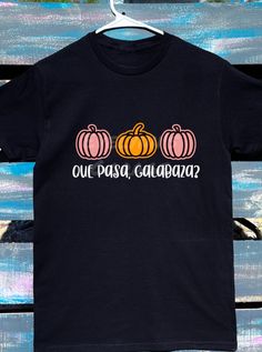 **Celebrate Halloween with a Twist of Mexican Tradition Introducing our personalized "Que Pasa Calabaza" Halloween shirt, where festive fun meets rich cultural heritage. This unique design features vibrant pumpkins and the playful phrase "Que Pasa Calabaza," blending the spooky spirit of Halloween with the warmth and charm of Mexican tradition. Perfect for those who want to stand out and embrace their roots while enjoying the season. Each shirt is crafted with care, using high-quality materials that ensure comfort and durability. Available in various sizes, it's a must-have for your Halloween wardrobe or a thoughtful gift for friends and family who love a touch of tradition. Celebrate the season in style--order your personalized "Que Pasa Calabaza" shirt today and bring a little bit of Mex Fun Black Shirt As Gift, Fun Black Shirt As A Gift, Casual Halloween T-shirt For Gift, Fun Black Customizable Shirt, October Shirts, Mexican Shirt, Spanish Shirts, Mexican Traditions, Mexican Shirts