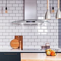 a kitchen with white tiled walls and wooden counter tops, hanging lights over the stove