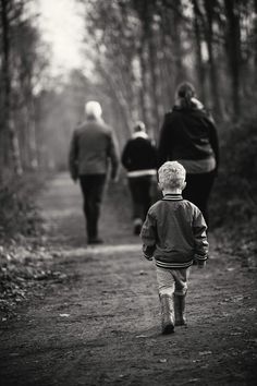 a little boy walking down a dirt road with two women behind him and an older woman in the background