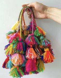 a hand holding a multicolored bag with tassels hanging from it's handle