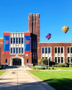 two hot air balloons are flying in the sky over a building with windows and grass