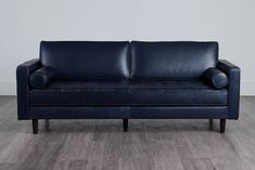 a blue leather couch sitting on top of a hard wood flooring covered floor next to a white wall