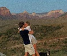 two people hugging each other while standing on top of a hill with mountains in the background