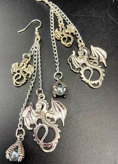 Unique and unusual dragon charm earrings. Adorned with gothic dragon charms and a glass pearl in a dragons talons. There are lightweight earrings which are nickel free and silver plated. They are about 4 inches long. These make a great gift idea! Gothic Metal Jewelry With Dragon Design, Fantasy Metal Single Earring, Punk Metal Jewelry For Fantasy Events, Fantasy Style Metal Single Earring, Silver Dangle Fantasy Earrings, Handmade Metal Fantasy Earrings, Handmade Fantasy Metal Earrings, Fantasy Dangle Earrings For Halloween, Halloween Fantasy Dangle Earrings