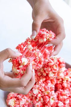 two hands reaching for popcorn that is being made into something red and white with sprinkles