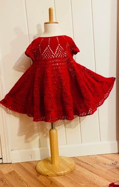 a red dress sitting on top of a wooden mannequin next to a white wall