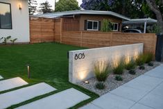 a modern home with grass and landscaping in the front yard at dusk, along with steps leading up to an address sign