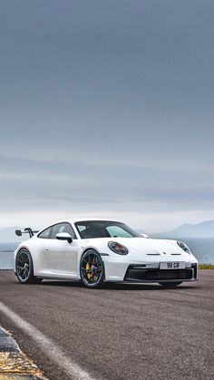 a white sports car driving down a road next to the ocean on a cloudy day