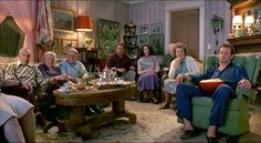 a group of older people sitting around a living room with food on the coffee table