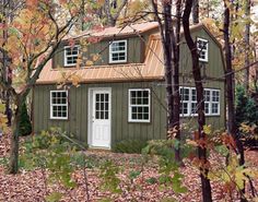 a small green house in the woods surrounded by trees and leaves with fall colors around it