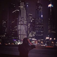 a person standing in front of a city skyline at night with their cell phone up to their ear