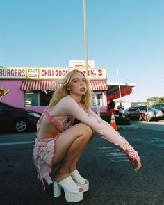 a woman sitting on top of a white bench in front of a building with a pink and white striped awning