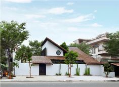 two people standing in front of a white building with a thatched roof and trees