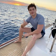 a young man sitting on the deck of a boat giving the peace sign with his hand