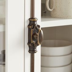 a close up of a door handle on a white cabinet with dishes in the background