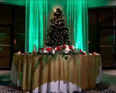 a christmas tree is lit up in the middle of a banquet room with green drapes