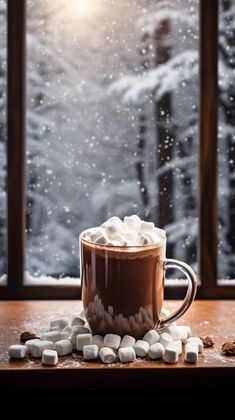 hot chocolate with marshmallows in front of a snowy window on a wooden table