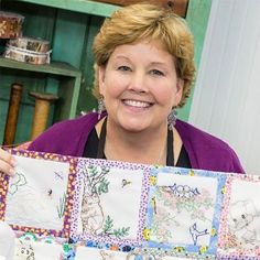 a woman is holding up a quilt with animals on it and smiling at the camera