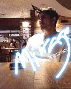 a man sitting at a table with a neon sign in front of him