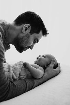 a black and white photo of a man holding a baby in his lap while looking down at him