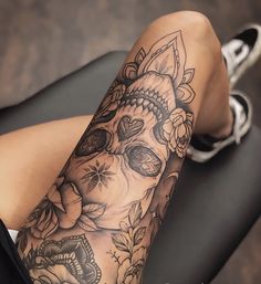 a woman's leg with a skull and flowers tattoo on her arm, sitting in a chair