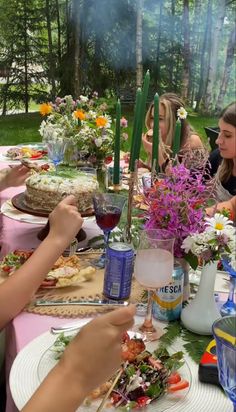 a group of people sitting around a table with food and drinks on it in the woods