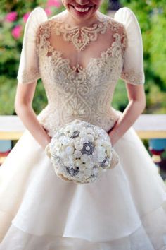 a woman in a wedding dress holding a bouquet with flowers on her hand and smiling at the camera