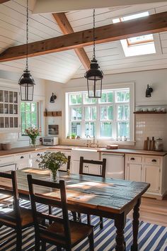 a table and chairs in a room with wooden beams on the ceiling, windows over the kitchen