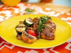 a yellow plate topped with meat and veggies on top of a red and white table