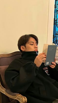 a man sitting on a couch reading a book with his eyes closed and head down