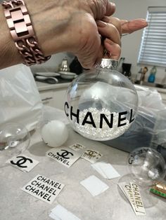 a person holding a chanel ornament on top of a table with other items