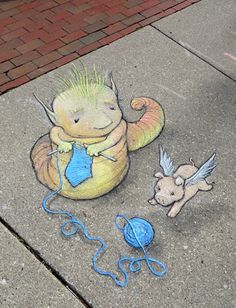 a chalk drawing of a baby dragon on the sidewalk next to a ball of yarn