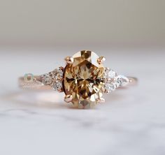 an engagement ring with a fancy brown diamond surrounded by white diamonds on a marble surface