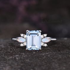 an aquamarine colored diamond ring with white diamonds on the sides and side stones around it