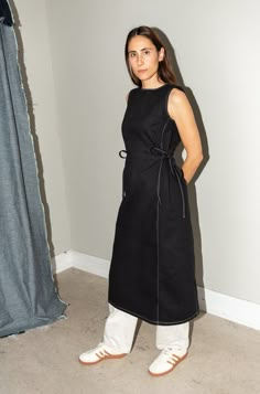 a woman standing in front of a curtain wearing white shoes and a black apron dress