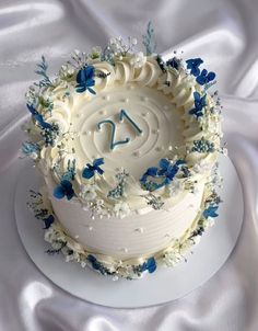 a white cake with blue and white flowers on it sitting on a white cloth covered tablecloth