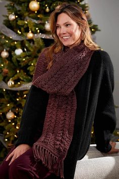 a woman sitting in front of a christmas tree wearing a burgundy scarf and black sweater