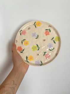 a hand holding a plate with flowers painted on the front and sides, against a white background