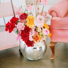 a vase filled with lots of different colored flowers on top of a table next to a pink chair