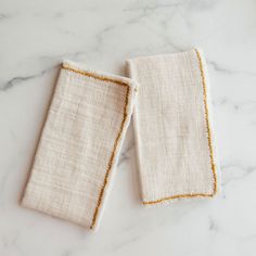 two linen napkins with gold trim on a marble surface