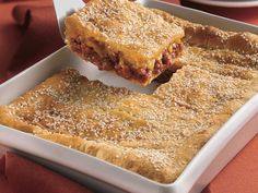 a square casserole dish filled with meat and cheese, being lifted by a spatula