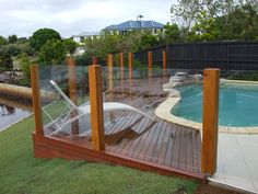 a wooden deck next to a pool with a chair on the side and fence around it