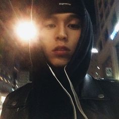 a young man wearing headphones standing in front of a building at night with the light shining on him