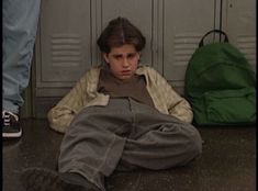 a young man sitting on the ground in front of lockers with his head down