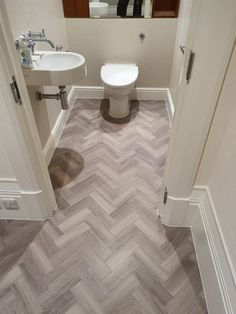 a white toilet sitting inside of a bathroom next to a sink on top of a wooden floor