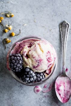 an ice cream sundae with berries and blueberries in it next to a spoon